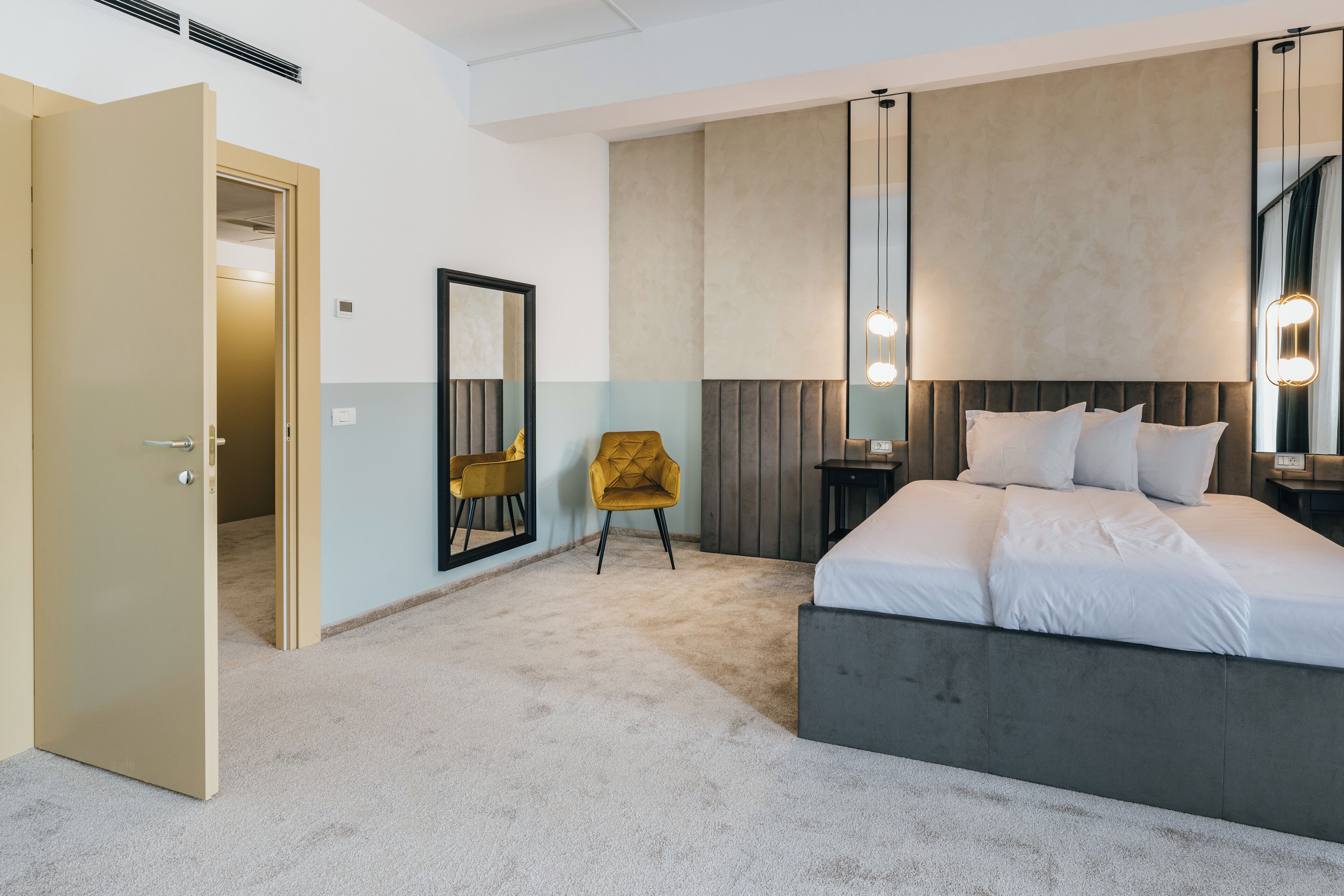 Une chambre d’hôtel moderne avec un grand lit, une chaise, une table de chevet et un miroir.