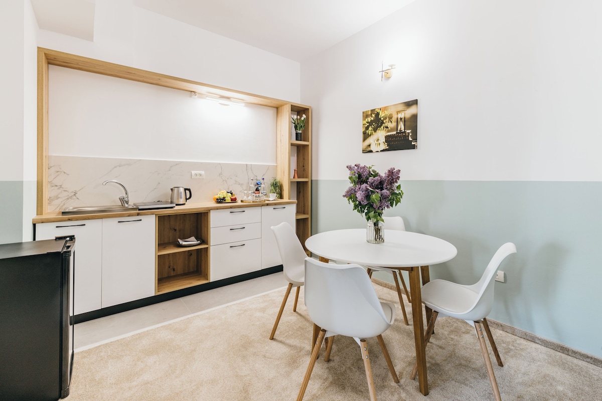 A compact kitchen with white cabinets, a wooden countertop, a sink, and a dining area with a white table and chairs.