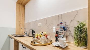 Une cuisine avec un plan de travail en bois, un pare-feu en marbre et une machine à café. On y trouve des fruits, des verres et une bouteille de Borsec sur le plan de travail.