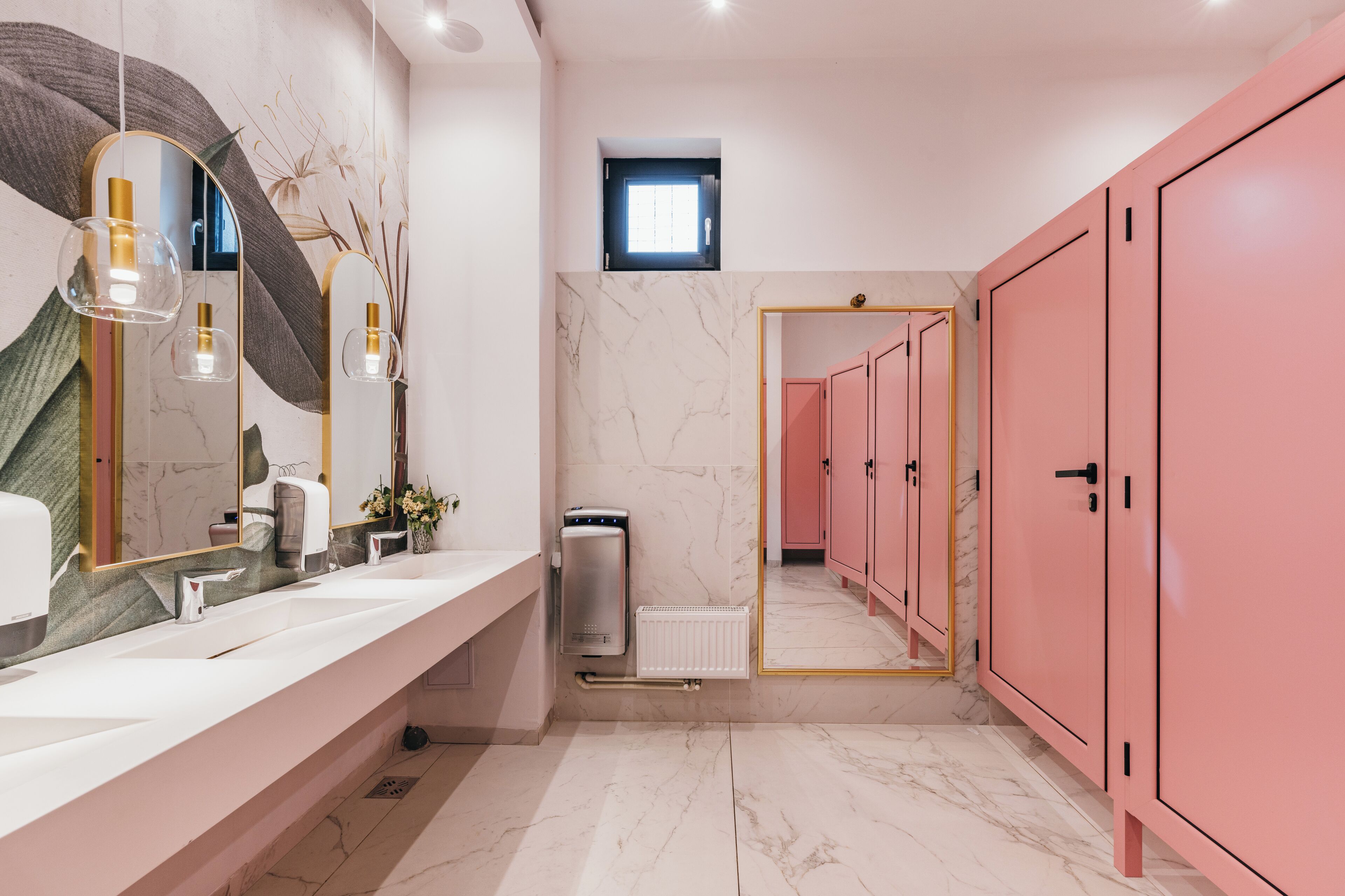 Un baño moderno con suelo de mármol blanco, un espejo grande, un lavabo blanco y armarios rosados.