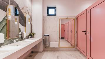 Un baño moderno con suelo de mármol blanco, un espejo grande, un lavabo blanco y armarios rosados.
