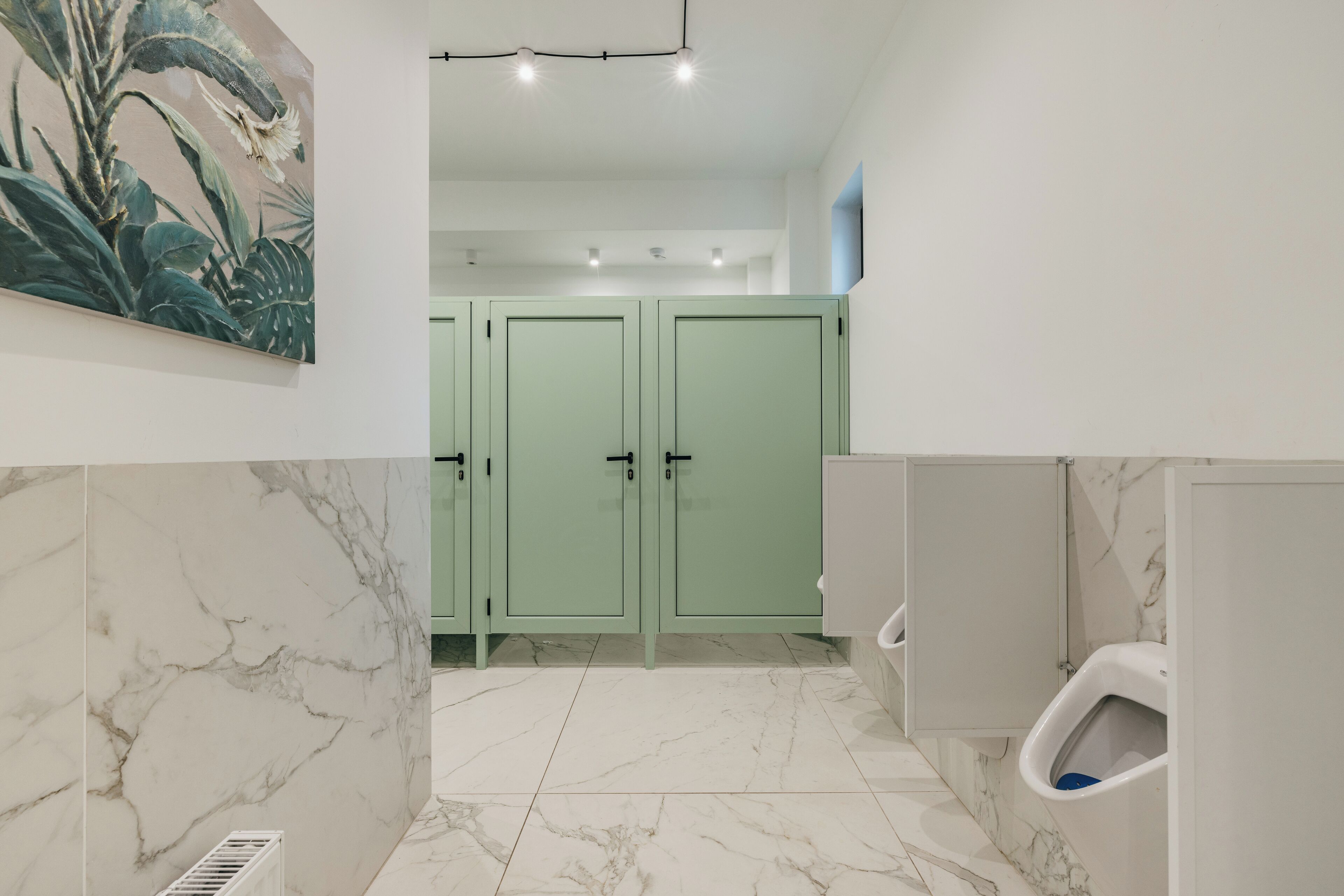 A bathroom with marble flooring, green cabinets, and a urinal.