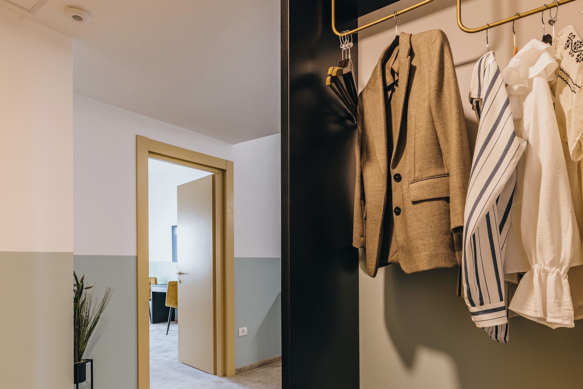 A hallway with a coat rack holding several jackets, a black bench, and a potted plant.