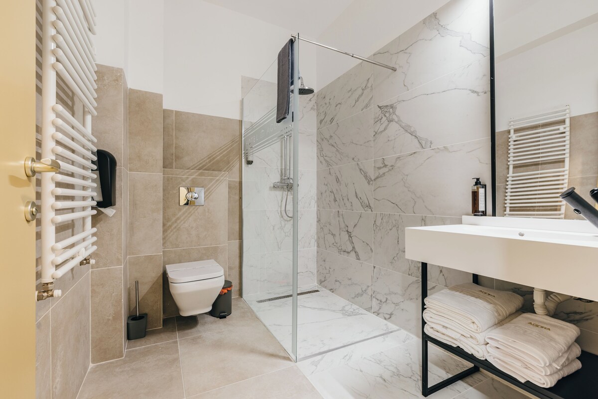 A modern bathroom with a glass-enclosed shower, a white sink, and marble tiles.