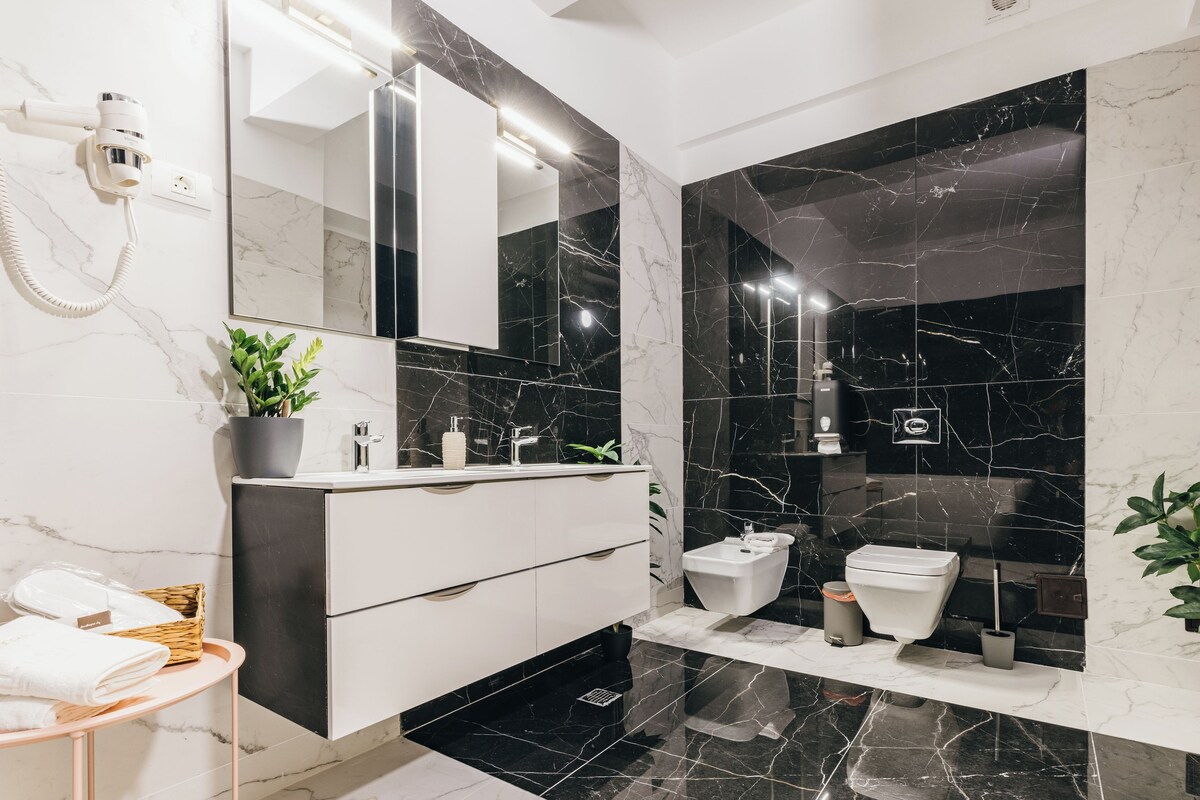 Un baño moderno con tocador blanco, salpicadero de mármol negro y un espejo grande.