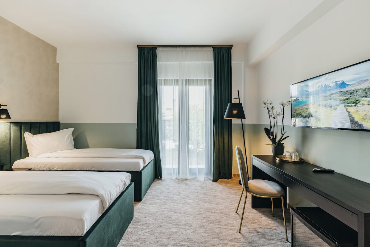 A hotel room with two beds, a desk, a chair, a TV, and a window with curtains.