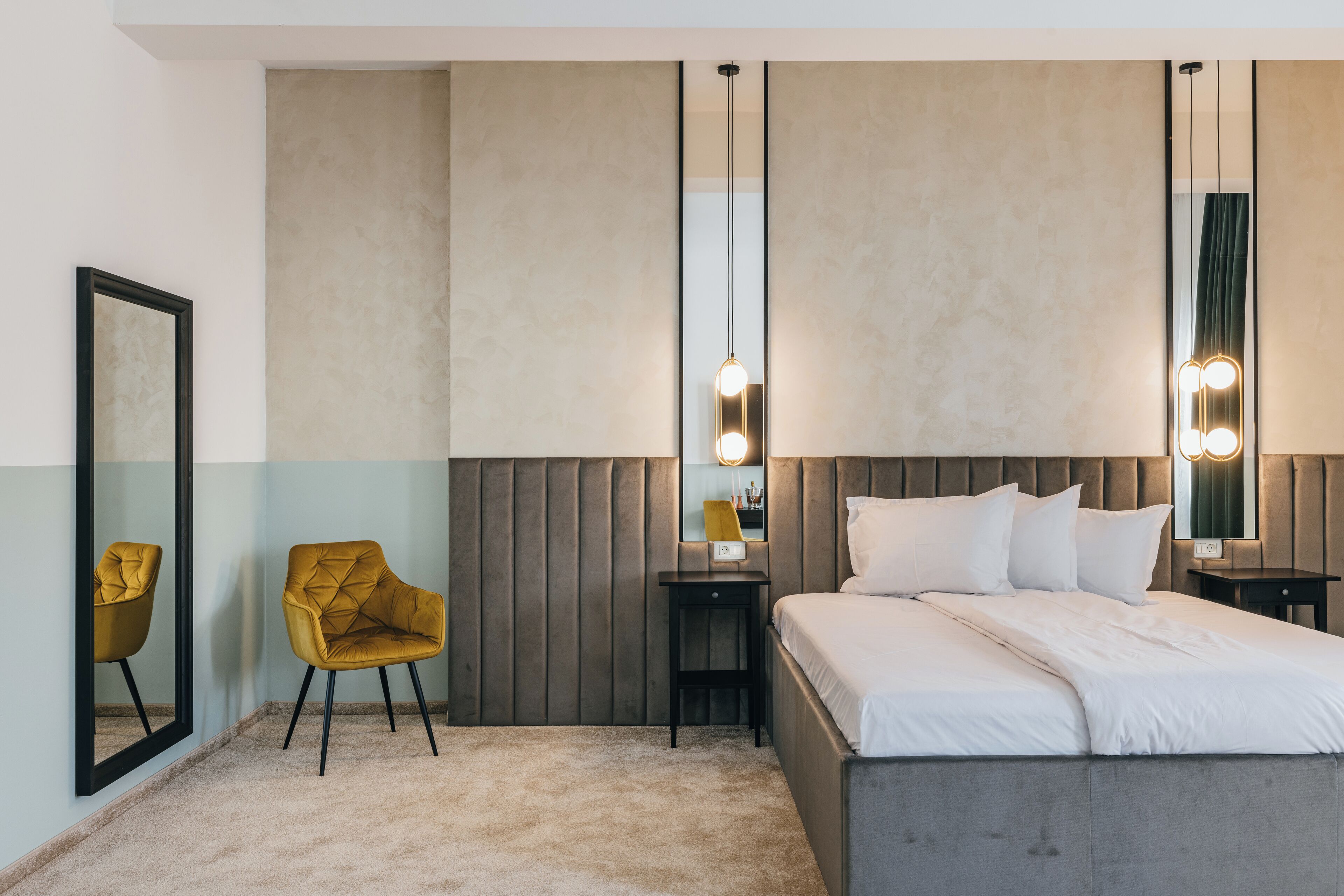 Ein modernes Hotelzimmer mit einem großen Bett, einem kleinen Nachttisch, einem Sessel und einem Spiegel.
