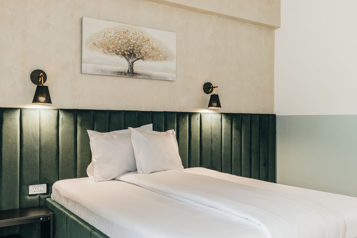 Una cama bien hecha con sábanas blancas y dos almohadas, un cabecero verde y dos lámparas de pared.