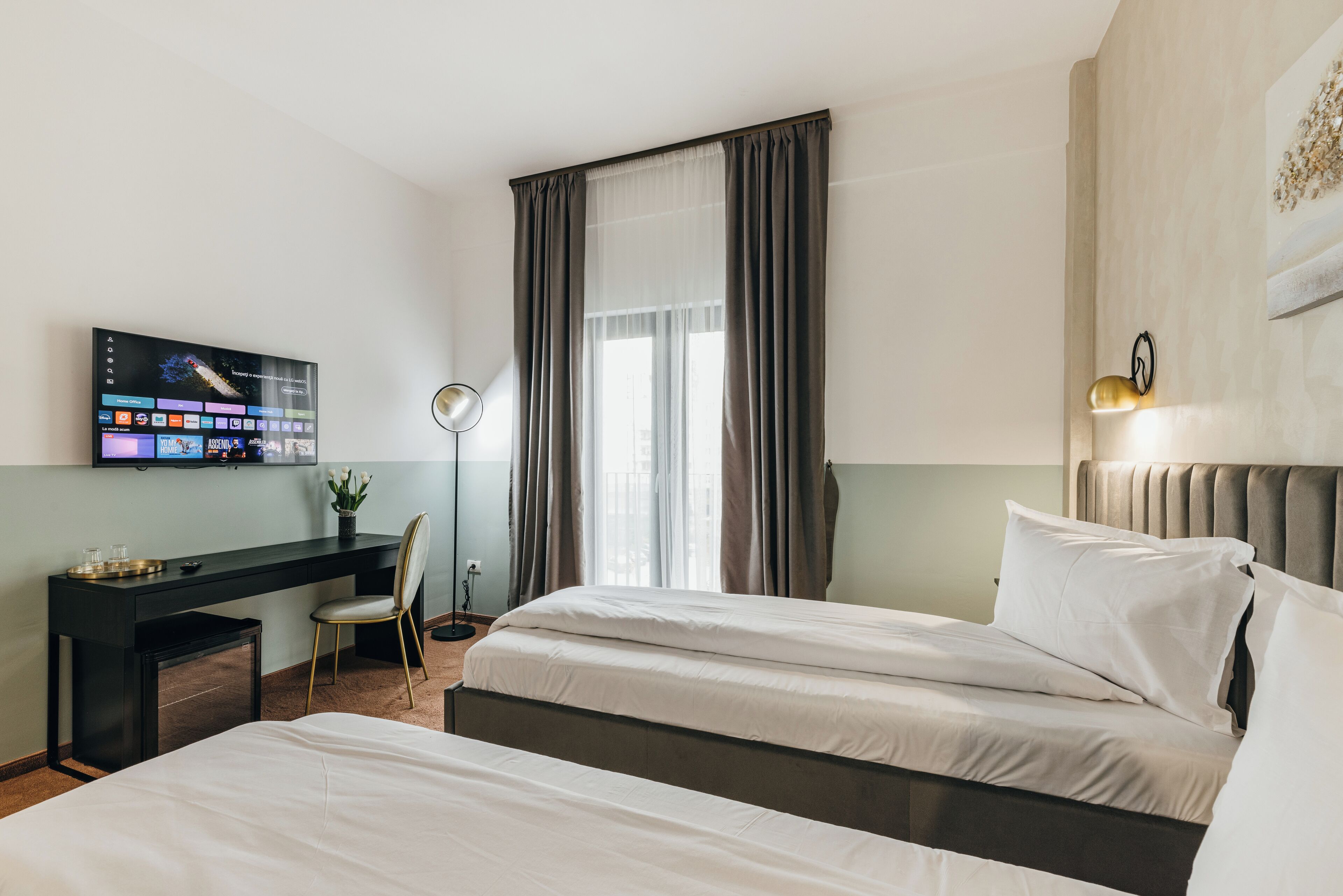 A hotel room with a bed, a desk, a TV, and a window with curtains.