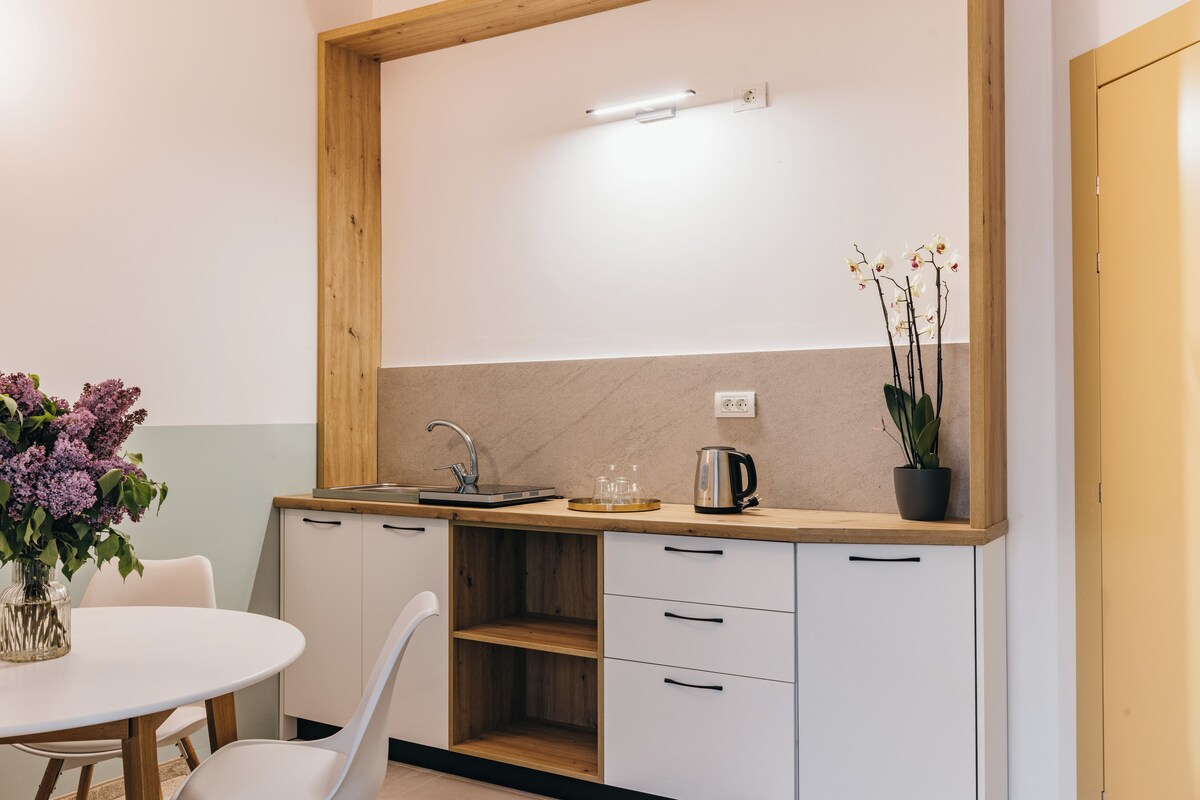 Una cocina compacta con encimera de madera, armarios blancos, un lavabo y una planta en maceta.
