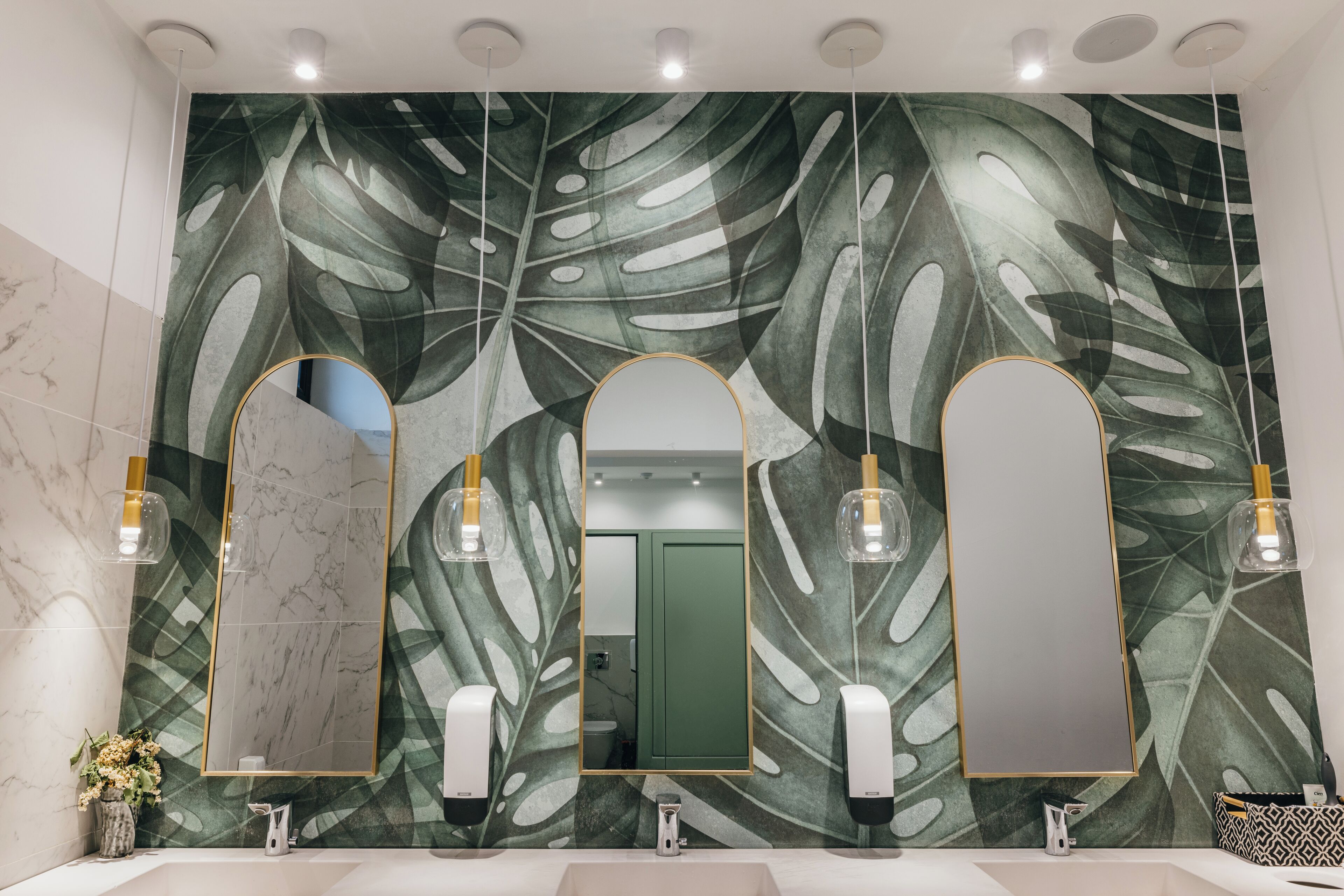 A bathroom with a large mirror, three pendant lights, and a wall with a leaf pattern.