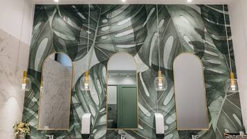 A bathroom with a large mirror, three pendant lights, and a wall with a leaf pattern.