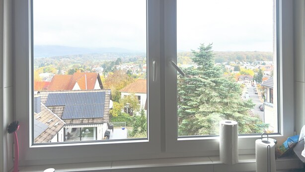 A room with two large windows offering views of a residential area with houses and trees. - Apartment Kelkheim (Kelkheim (Taunus))