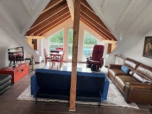 A loft-style room with a dining area, a massage chair, a sofa, and a TV.