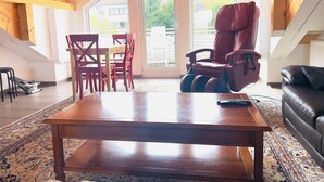 A spacious loft with a high ceiling, wooden beams, a large sliding glass door, a red leather chair, a black leather sofa, and a wooden coffee table. - Apartment Kelkheim (Kelkheim (Taunus))