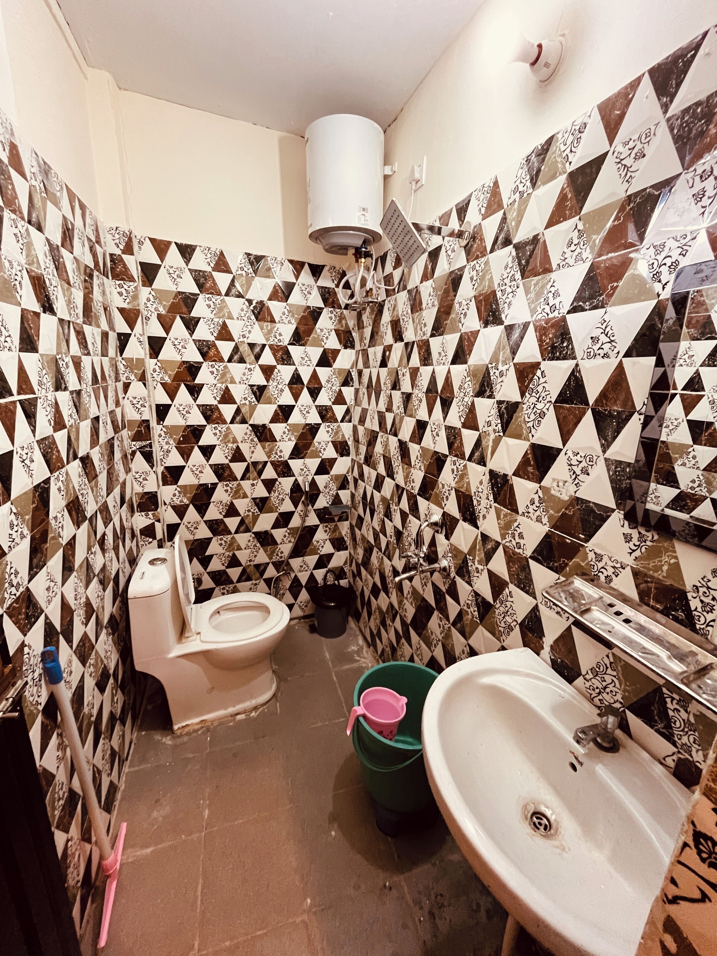 A bathroom with a toilet, sink, and shower. The walls are tiled with a geometric pattern.