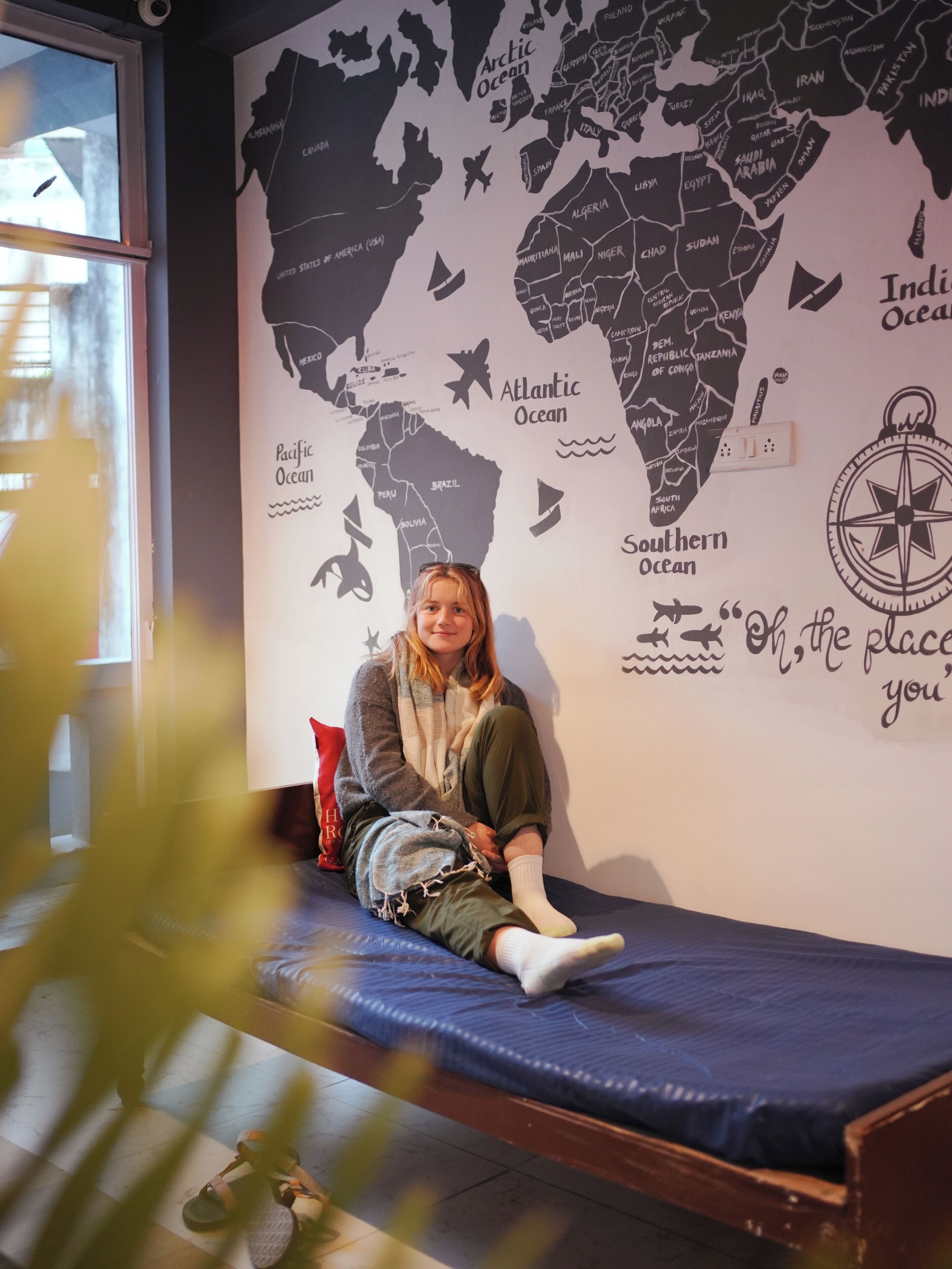 Una persona sentada en una cama, con un mural de un mapa mundial en la pared de fondo.