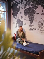 Una persona sentada en una cama, con un mural de un mapa mundial en la pared de fondo.