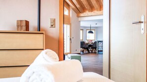 A hotel room with a wooden bed, a neatly made bed with a rolled white towel, a wooden dresser, and a view into the dining area with a table and chairs. - Beautiful apartment for 6 guests with WIFI, TV and terrace (Basse-nendaz)