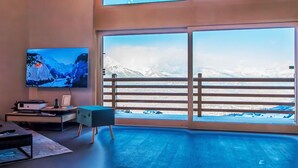 A modern living room with a large TV, wooden flooring, and a balcony with a mountain view. - Beautiful apartment for 6 guests with WIFI, TV and terrace (Basse-nendaz)