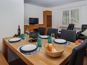 Een eethoek met een houten tafel voor vier personen, een televisie op de achtergrond en een raam met uitzicht.