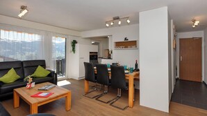 Uma sala de estar moderna com um sofá preto, mesa de centro de madeira e área de jantar com cadeiras e mesa.