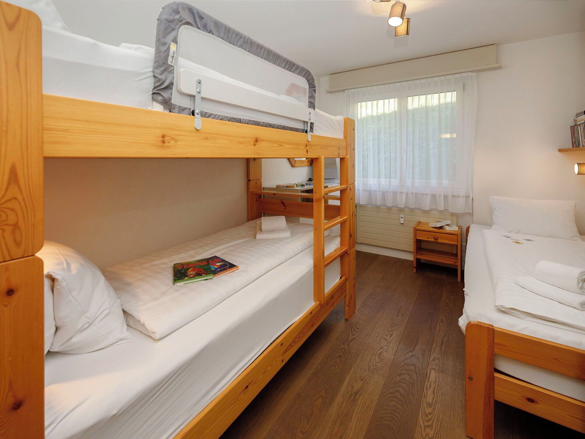 Een slaapkamer met stapelbed, bureau, een klein tafeltje en een raam met gordijnen.