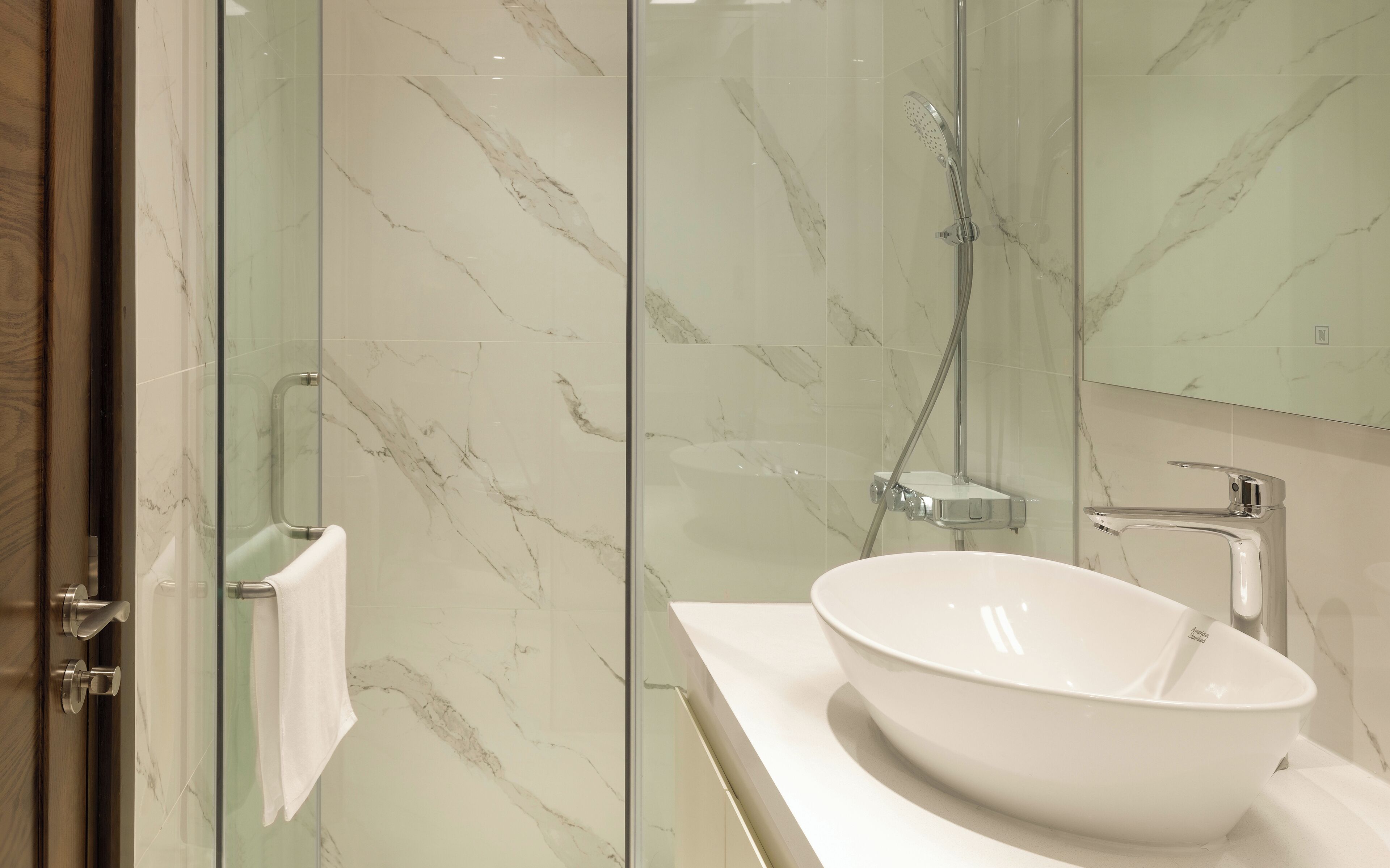 A modern bathroom with a glass shower enclosure, a white sink, and a marble backsplash.