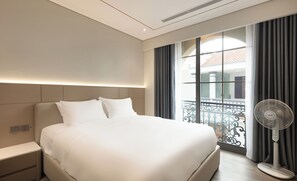 Een hotelkamer met een groot bed, een nachtkastje, een wandlamp, een raam met gordijnen en een staande ventilator.