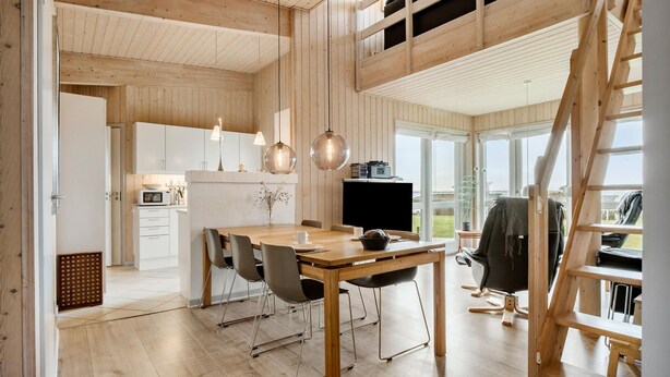 Een ruime keuken met houten kastjes, een eethoek met een houten tafel en stoelen, en een groot raam met uitzicht op de omgeving.