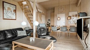 Een moderne woonkamer met een zwarte leren bank, een houten salontafel en een eethoek met een houten tafel en stoelen.