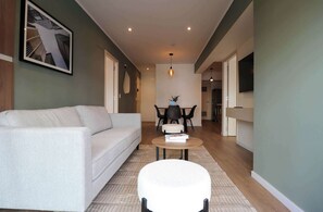 A modern living room with a sofa, a round coffee table, and a white ottoman. There is a dining area with a table and chairs in the background. - w* | Grandiosel 2BR in Miraflores Near Larcomar (Miraflores)