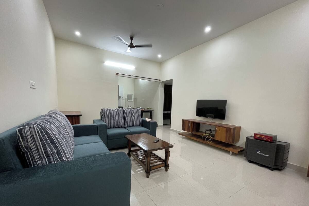 Un salon moderne avec un canapé, une table basse, un téléviseur posé sur un meuble en bois et un ventilateur de plafond.