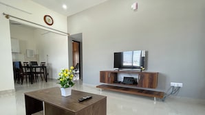 A modern living room with a wooden coffee table, a flat-screen TV on a wooden stand, and a dining area with a table and chairs.