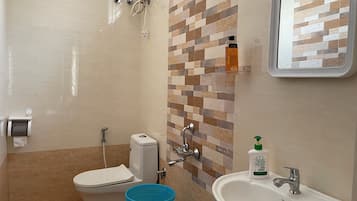 Un baño con inodoro, ducha, lavamanos y un cubo azul.