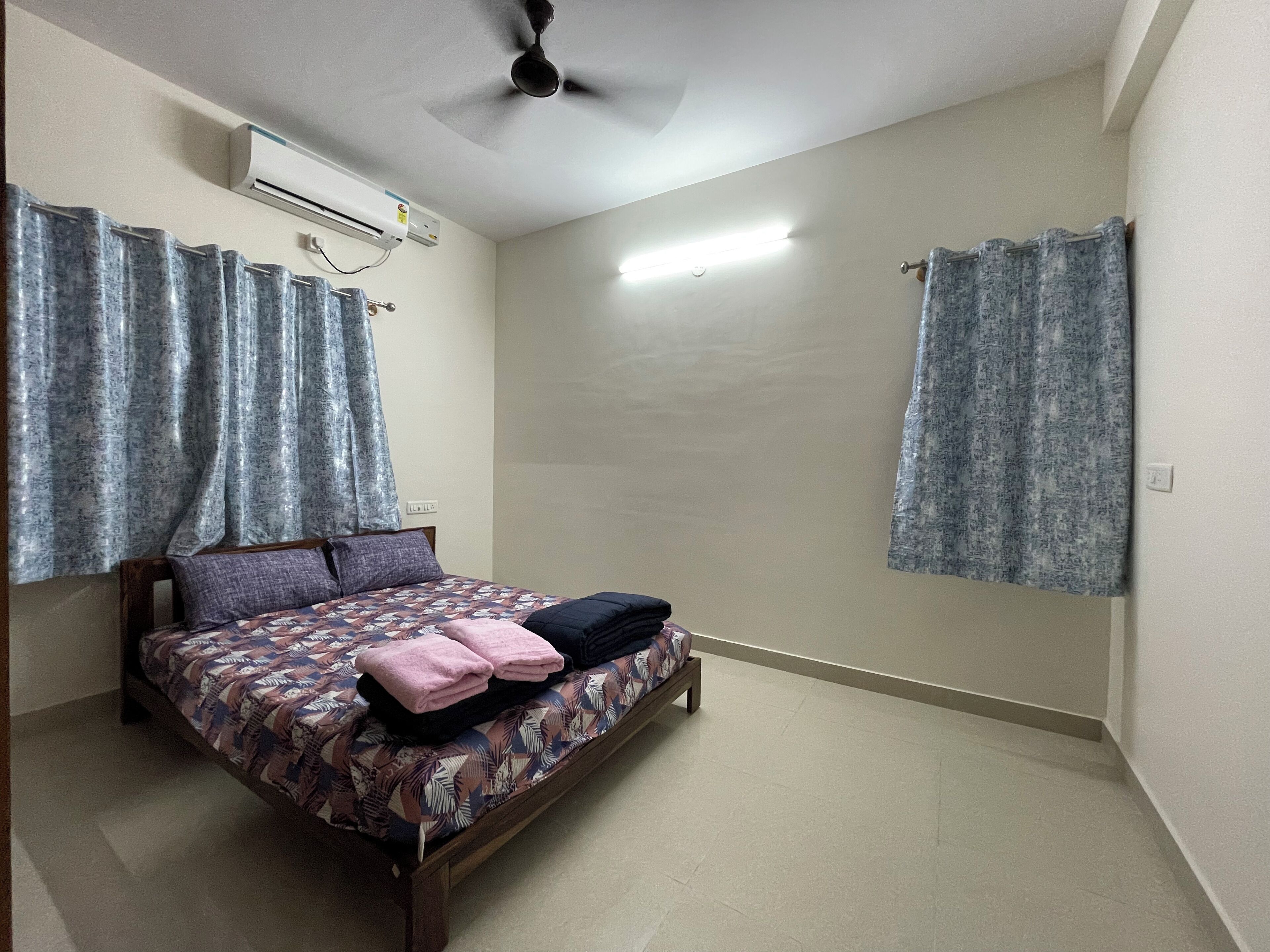 A bedroom with a bed, curtains, an air conditioning unit, and a ceiling fan.