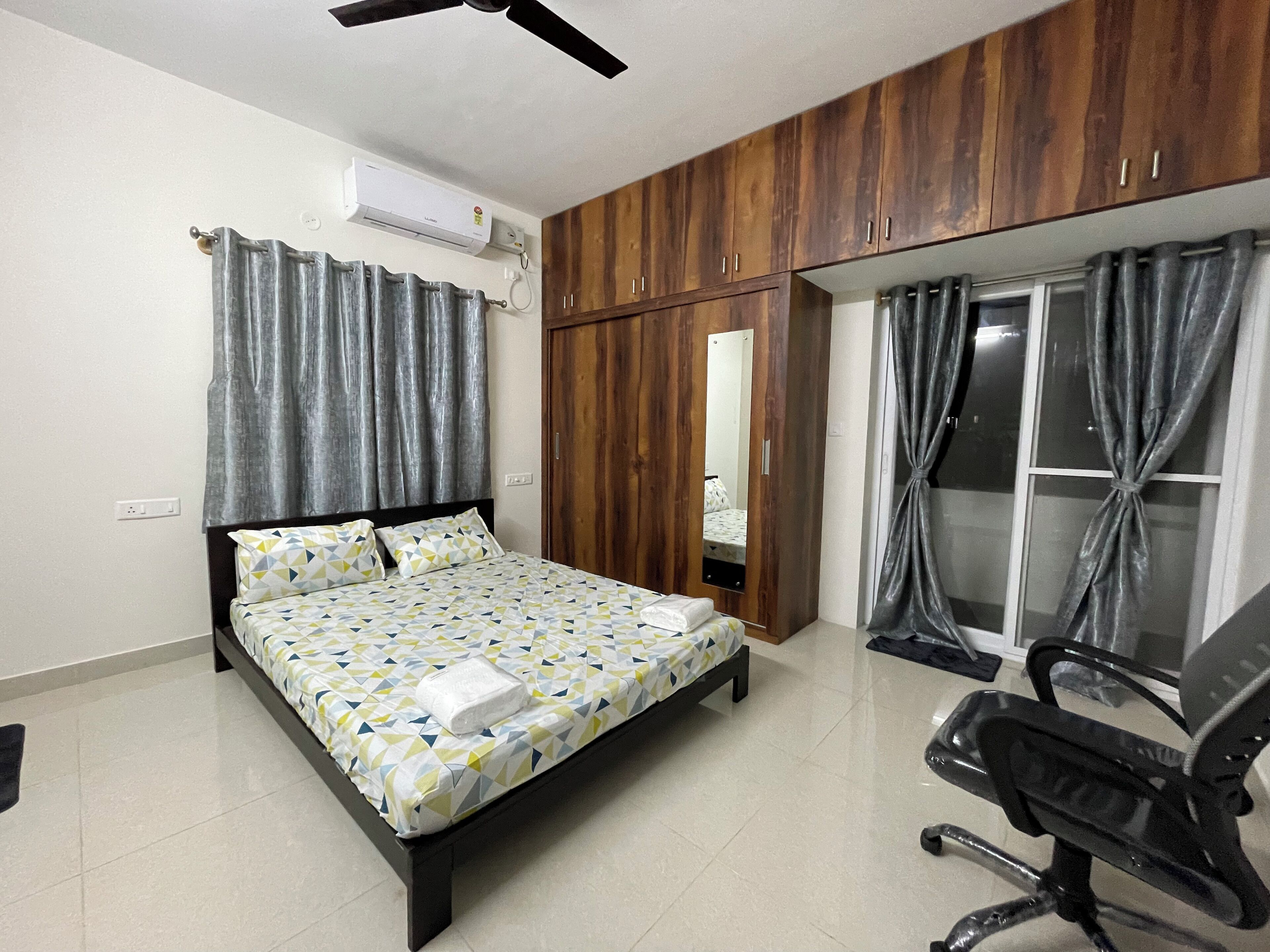 A bedroom with a bed, a desk, a chair, a wardrobe, and a window with curtains.