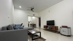 A modern living room with a grey sofa, a coffee table, a flat-screen TV on a wooden stand, and a Vachhmann storage unit.