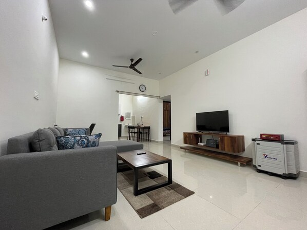 Un salón moderno con un sofá gris, una mesa de centro, un televisor de pantalla plana sobre un soporte de madera y un mueble de almacenamiento Vachhmann.