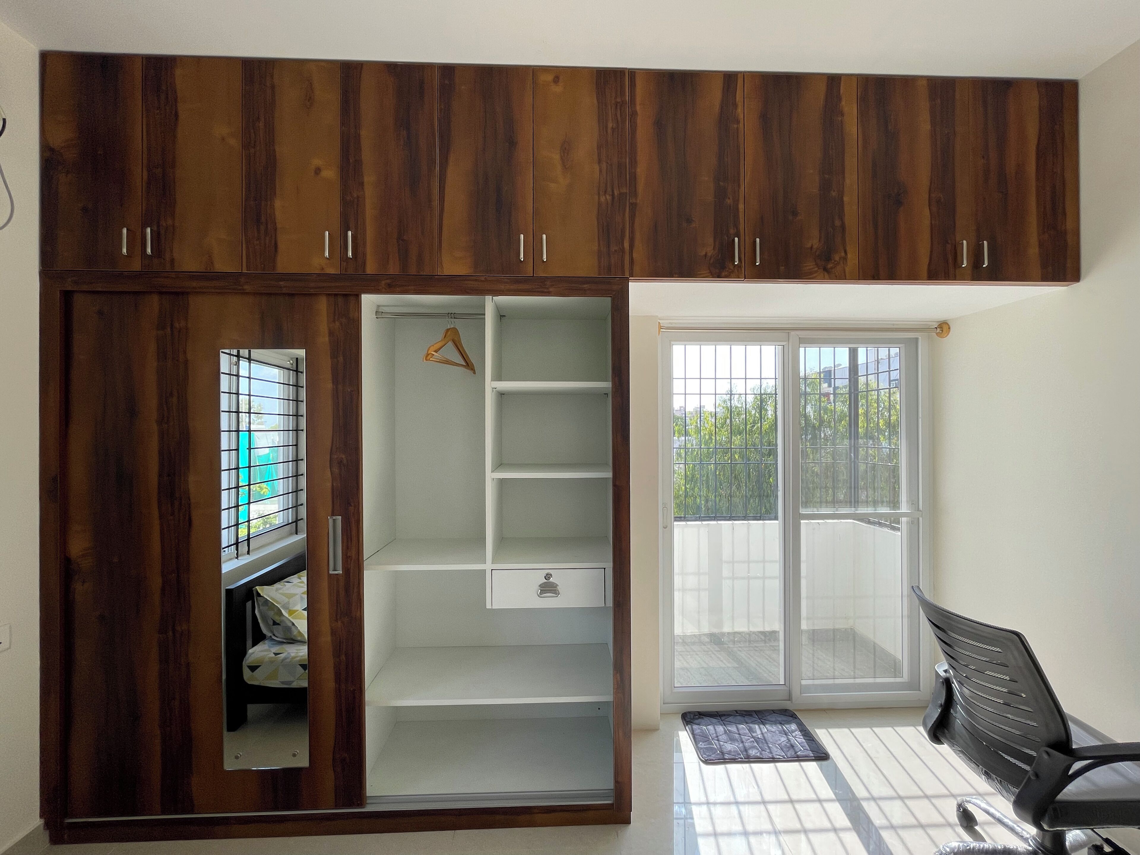 Una habitación con armario, escritorio y puerta corrediza de vidrio que da a un balcón.