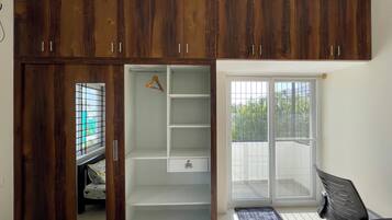 Una habitación con armario, escritorio y puerta corrediza de vidrio que da a un balcón.