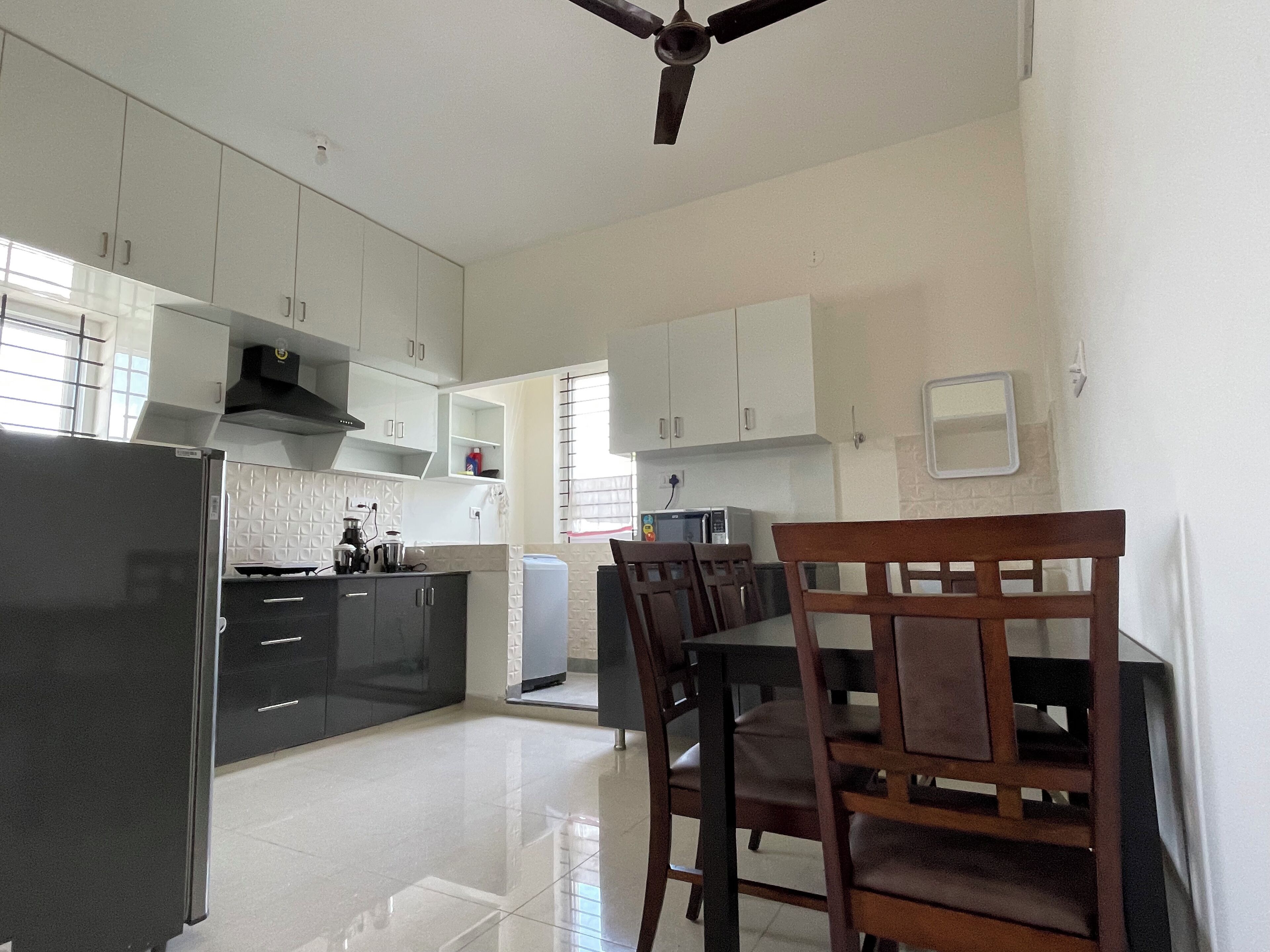 A modern kitchen with white cabinets, a black refrigerator, and a dining area with wooden chairs and a table.