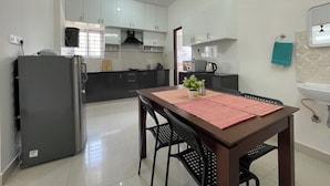 A modern kitchen with white cabinets, a black refrigerator, and a dining table with a red placemat.