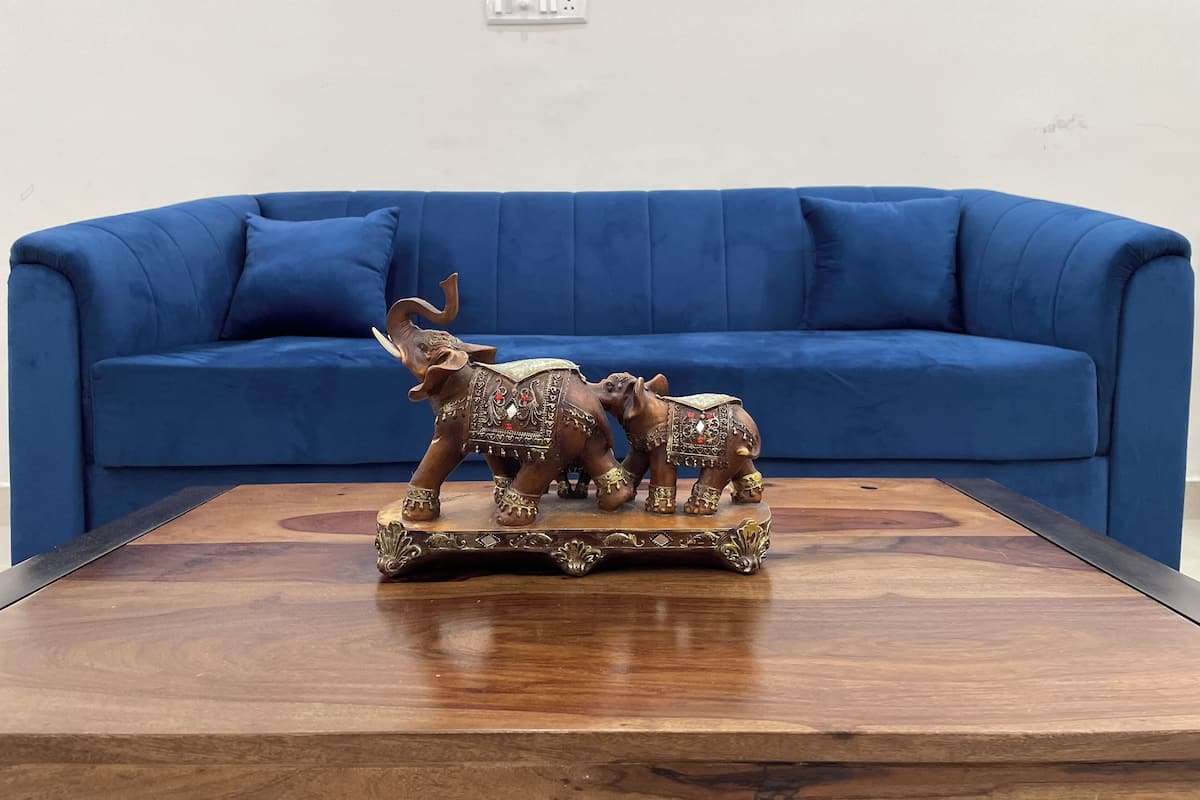 Un canapé bleu et une table basse en bois ornée d’une statuette d’éléphant décorative.