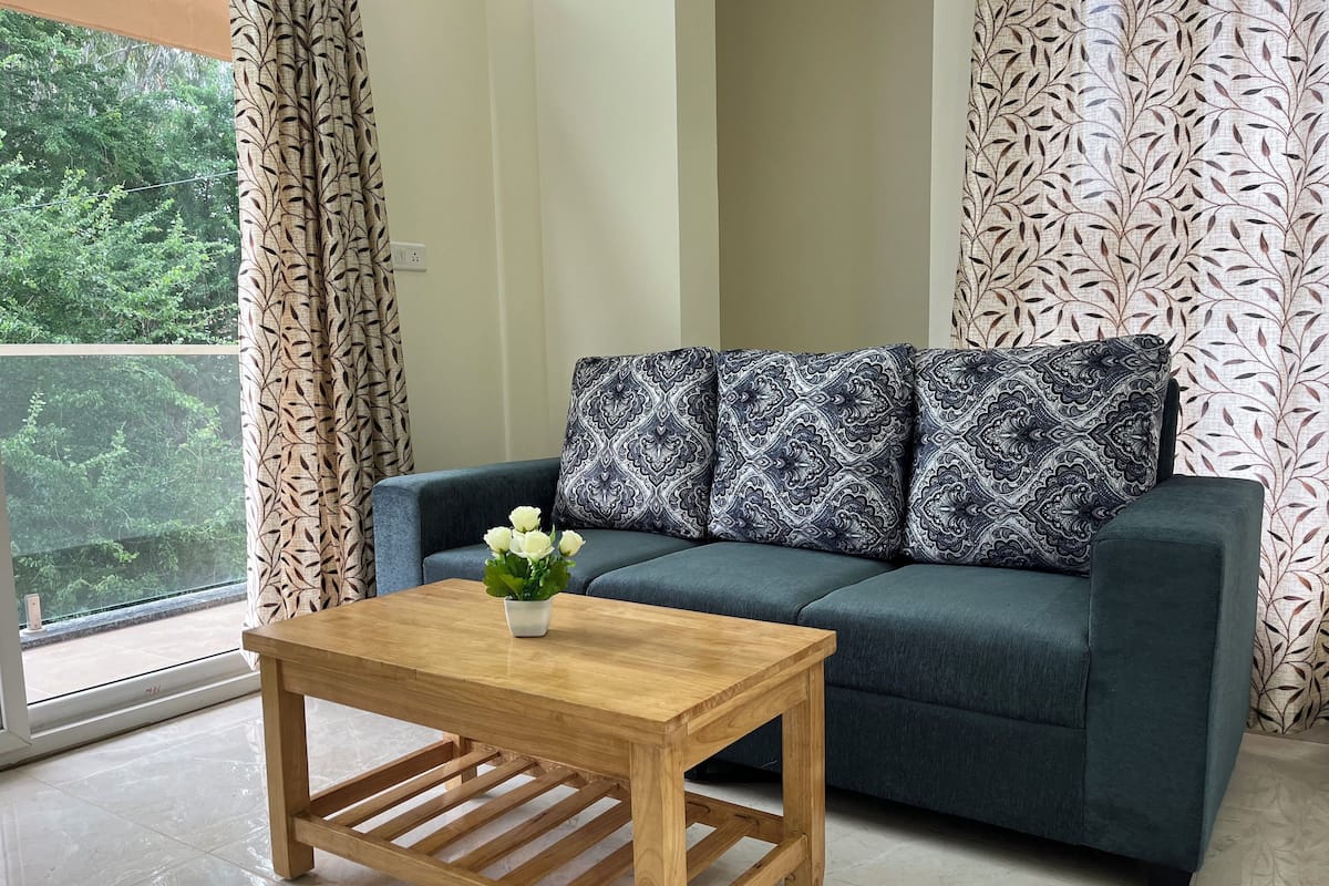 Un salon avec un canapé bleu foncé, des coussins à motifs, une table basse en bois et un vase rempli de fleurs blanches.