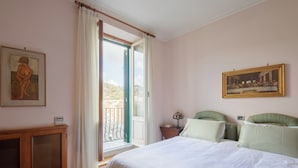 A bedroom with a bed, a nightstand, a lamp, a painting, and a window with curtains. - Bright and cozy apartment located in the heart of Rome, Vatican area.   (Roma)