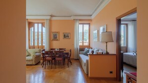 A spacious living area with a wooden floor, a dining table, a sofa, and a lamp. - Bright and cozy apartment located in the heart of Rome, Vatican area.   (Roma)