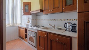 A kitchen with wooden cabinets, a stove, a sink, and a coffee maker. - Bright and cozy apartment located in the heart of Rome, Vatican area.   (Roma)