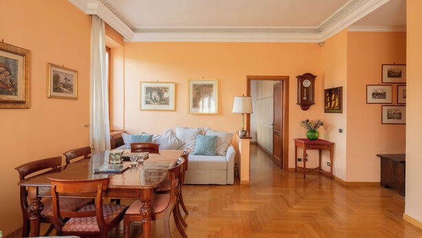 A dining area with a wooden table and chairs, a sofa, and a lamp. - Bright and cozy apartment located in the heart of Rome, Vatican area.   (Roma)