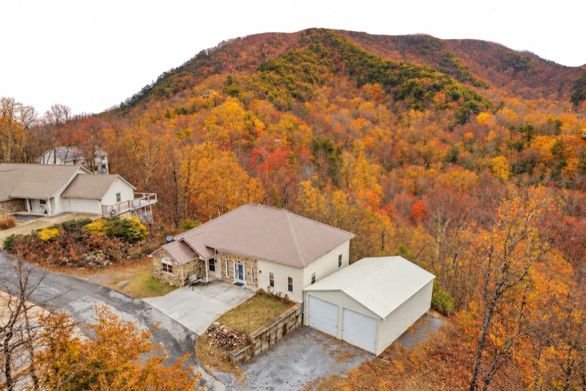 A residential area with a house featuring a garage, a driveway, and a hill with autumn foliage in the background.